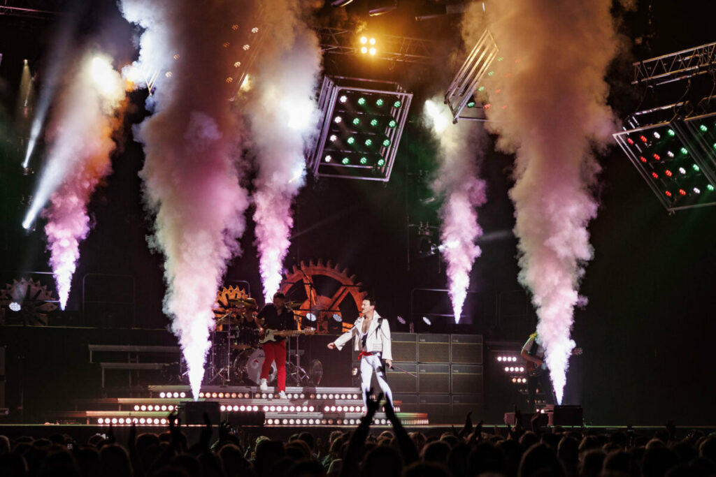 Concert en extérieur avec des effets lumineux et de la fumée, un artiste engage le public sur scène.