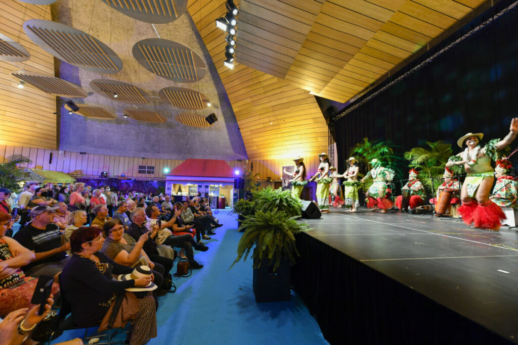 Spectacle de danse sur scène avec un public enthousiaste applaudissant. Ambiance festive et colorée.