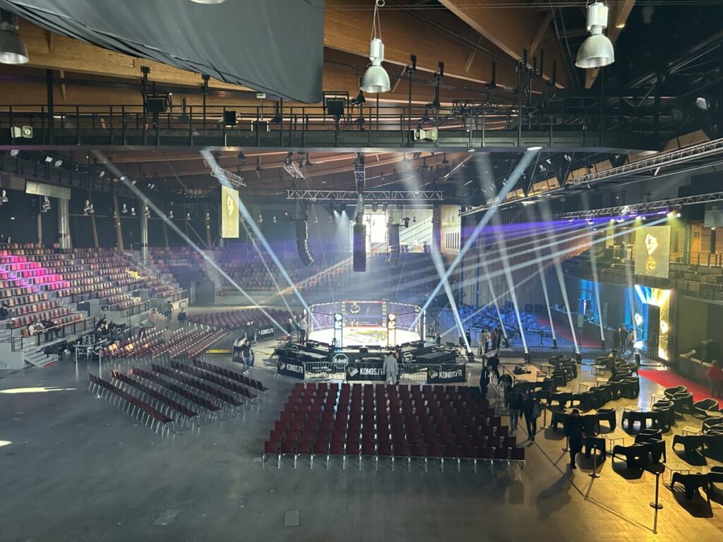 Salle de spectacle préparée pour un événement, avec une scène centrale et des sièges disposés autour.