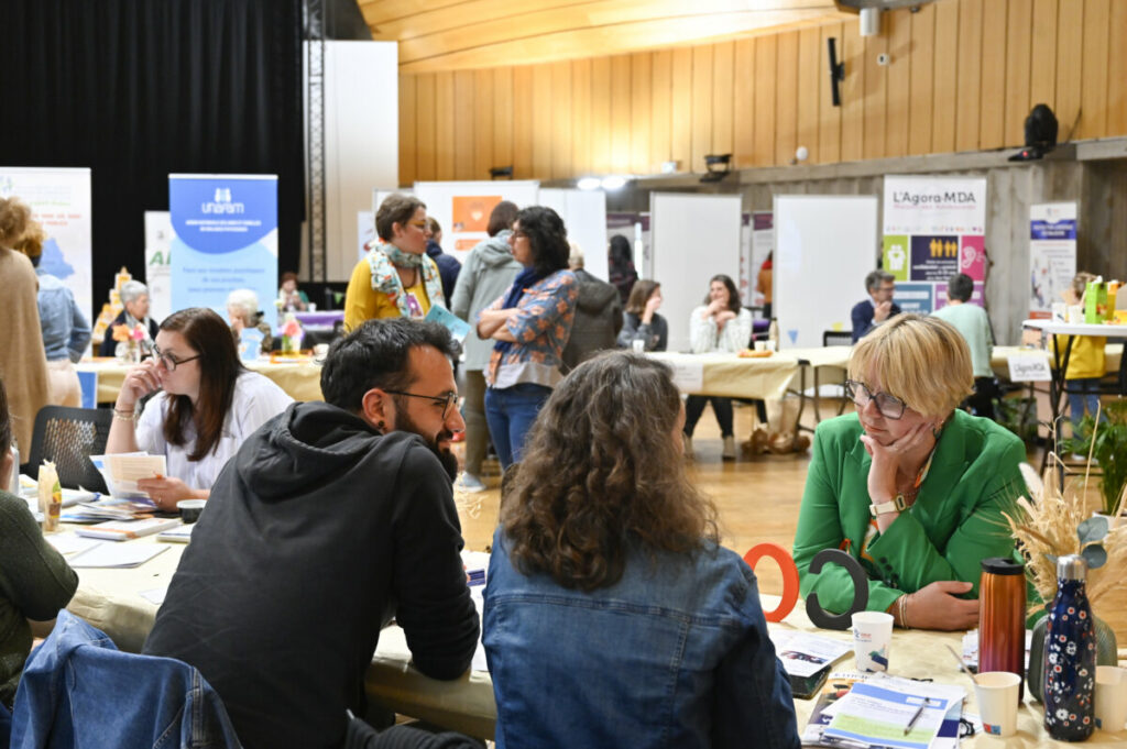 Participants discutent lors d'un événement, entourés de stands et de documents d'information.