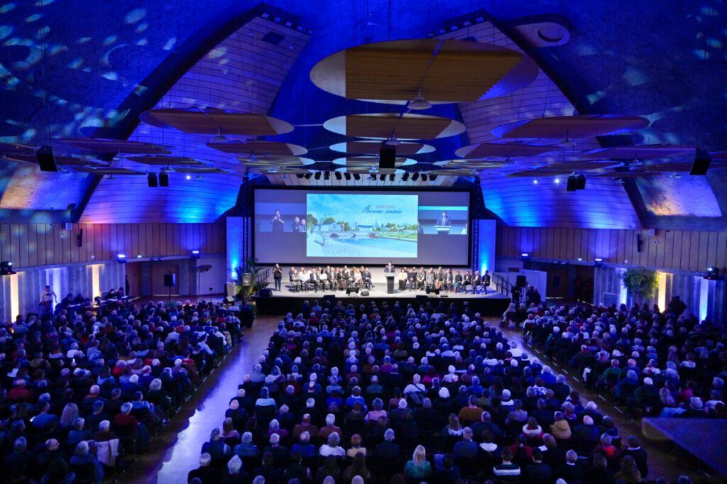 Cérémonie avec un orateur sur scène, devant un public attentif dans un grand auditorium éclairé.