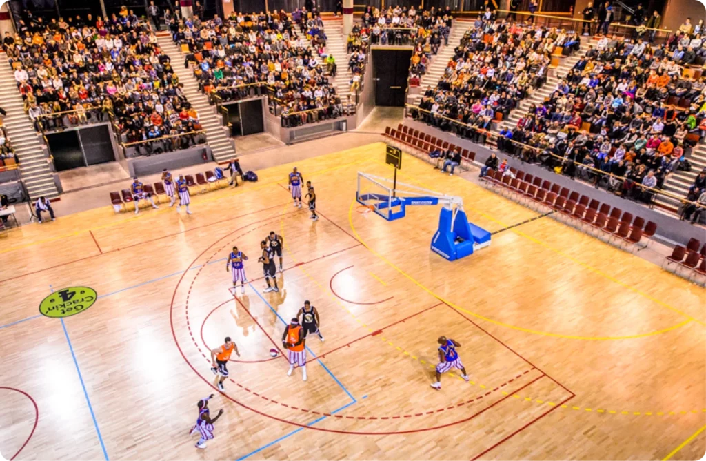 Match de basket-ball avec des spectateurs dans les gradins. Joueurs en action sur le terrain.