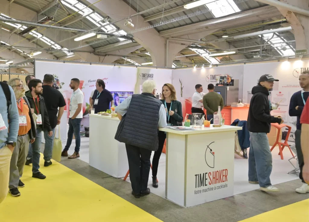 Un groupe de personnes discute autour du stand de TIME SHAKER lors d'un salon professionnel.