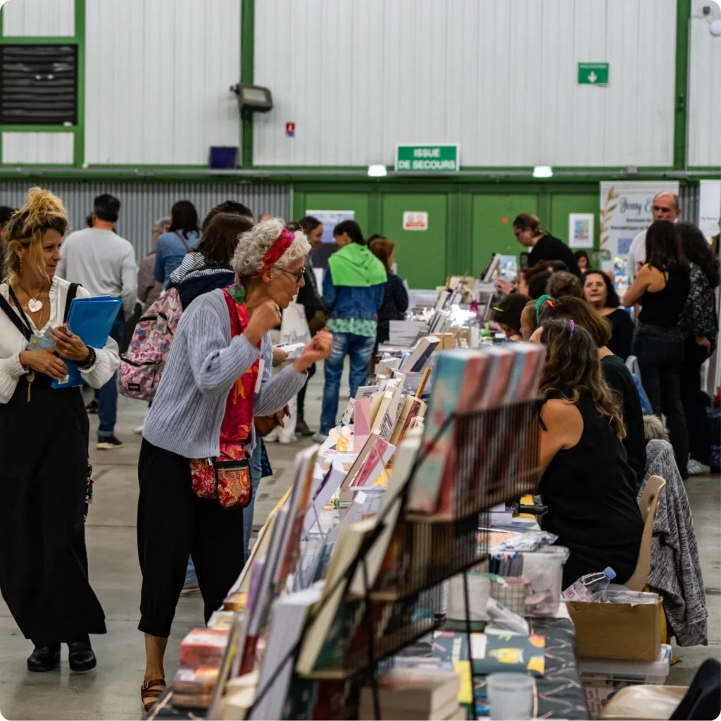 Foule animée dans un salon, avec des visiteurs explorant des stands de livres et d'artisanat.