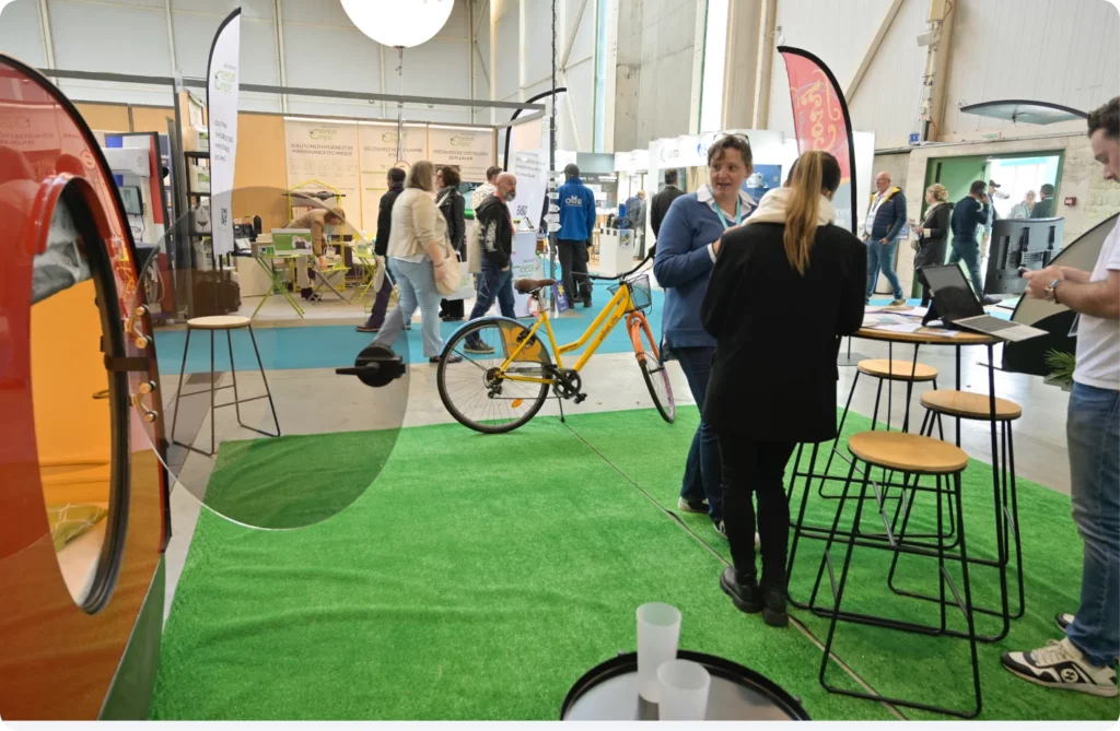 Échanges entre visiteurs à un salon, avec un vélo bien visible et des stands en arrière-plan.