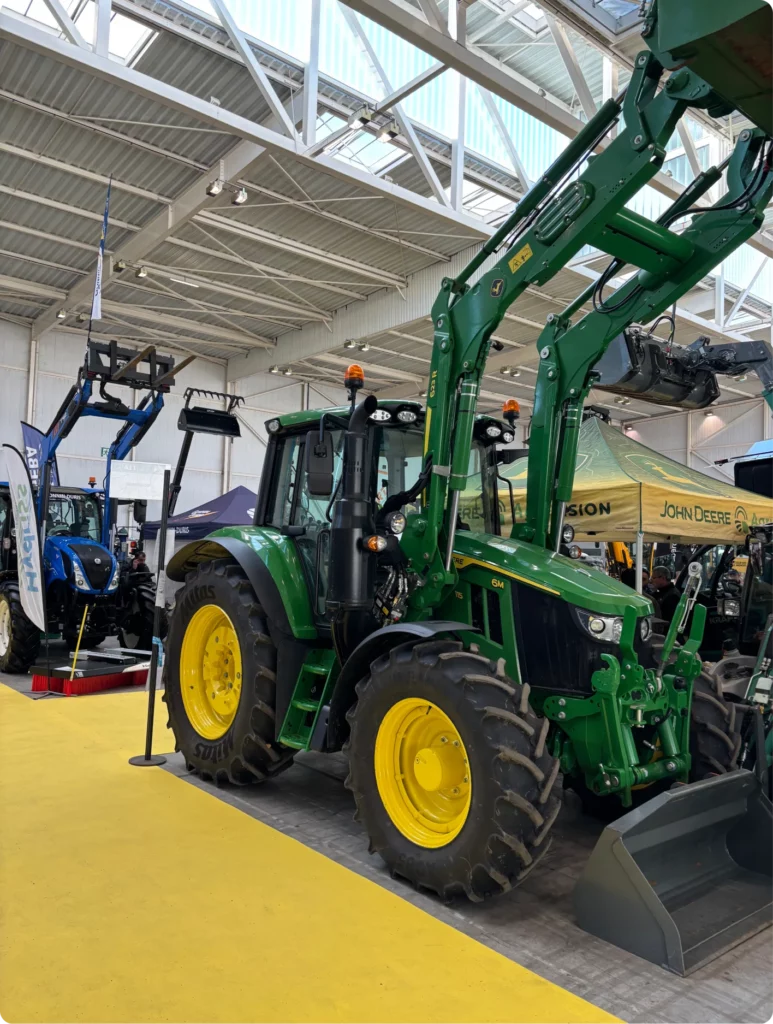 Tracteur vert exposé dans un salon, équipé d'un bras de levage et d'un godet.