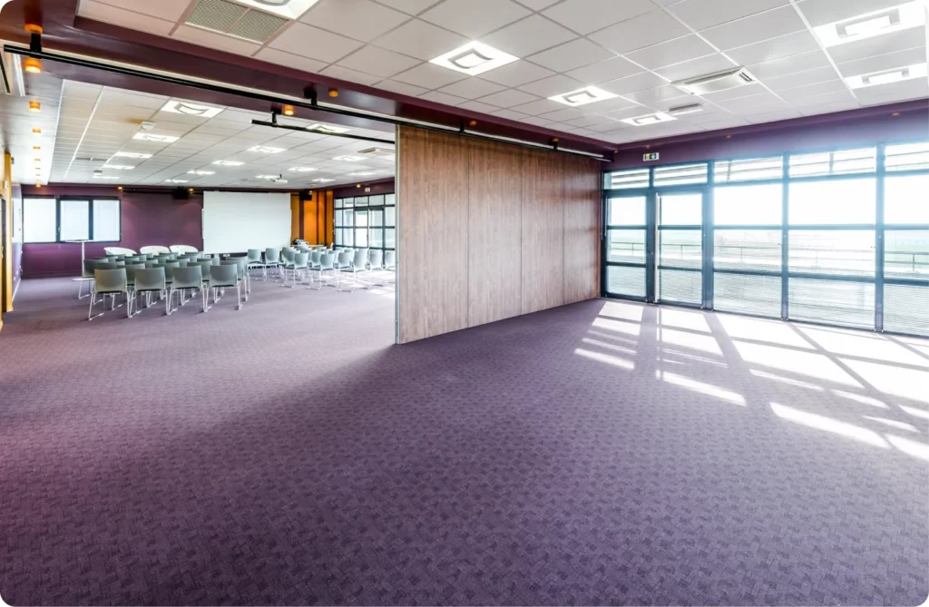 Salle de réunion spacieuse avec des sièges, éclairage naturel et une cloison mobile pour diviser l'espace.