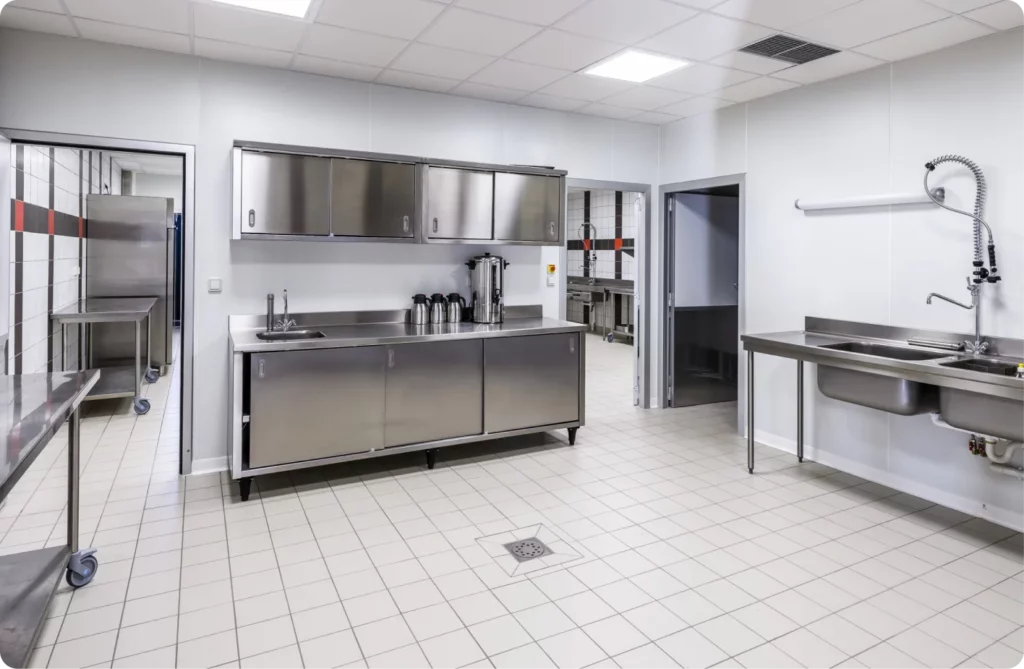 Cuisine professionnelle bien équipée avec des plans de travail en acier inoxydable et des lavabos.