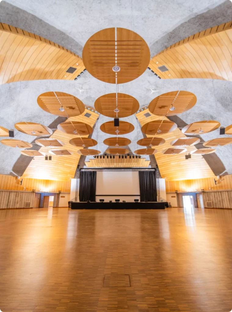 Salle de conférence spacieuse avec un grand écran et un plafond artistique en bois.