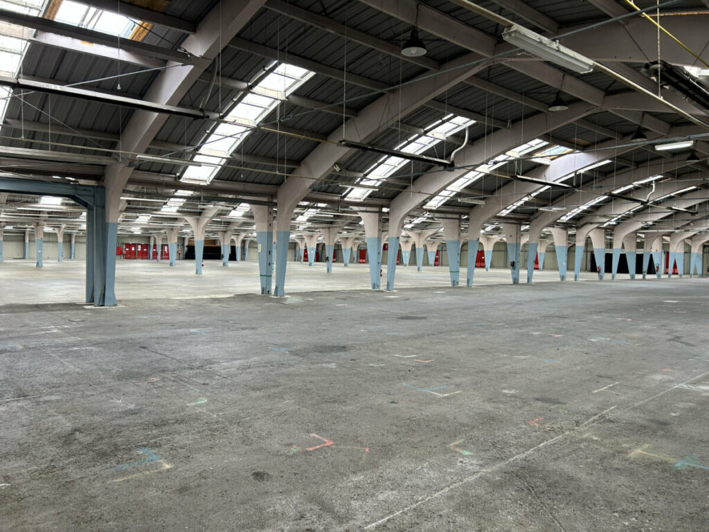 Grand espace intérieur d'un bâtiment avec des colonnes, éclairage naturel et murs de couleur neutre.